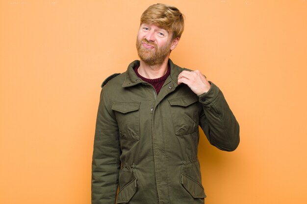 Young blonde man looking arrogant, successful, positive and proud, pointing to self against flat wall