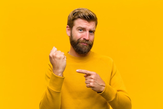 Young blonde man looking impatient and angry, pointing at watch