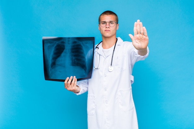 Young blonde man looking serious, stern, displeased and angry showing open palm making stop gesture