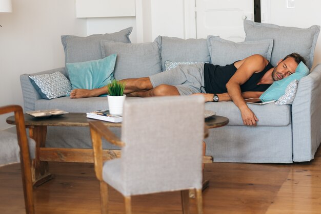 Young blonde man lying down in the couch at home sleeping