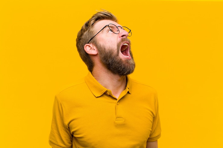 Photo young blonde man screaming furiously, shouting aggressively, looking stressed and angry against orange wall