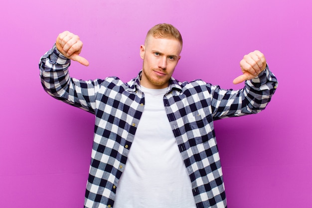 young blonde man showing thumbs down in disagreement