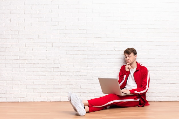 Young blonde man sitting on the floor with a laptop