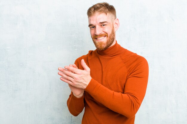 Giovane biondo che sorride e che applaude le mani