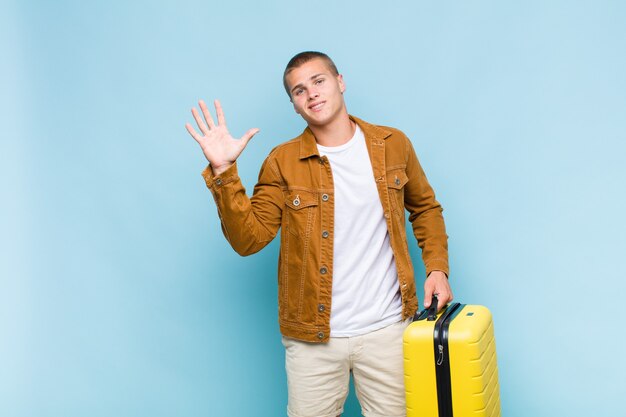 Young blonde man smiling happily and cheerfully, waving hand, welcoming and greeting you, or saying goodbye