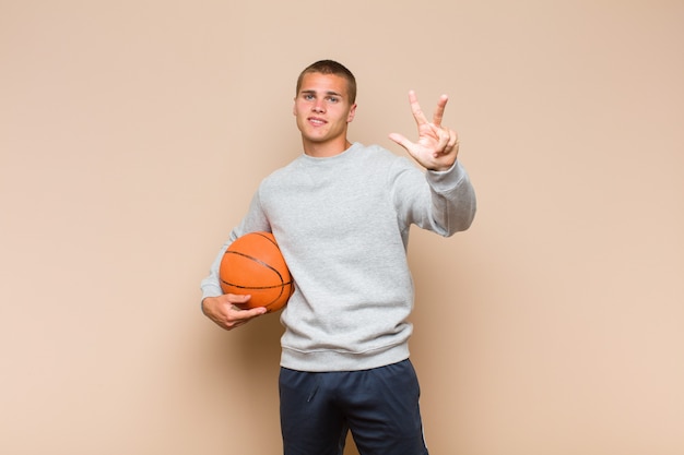 Young blonde man smiling and looking friendly, showing number\
one or first with hand forward, counting down