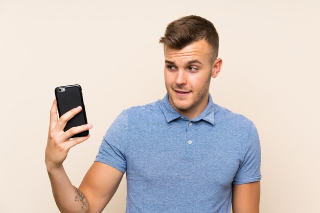 Young blonde man using mobile phone with happy expression