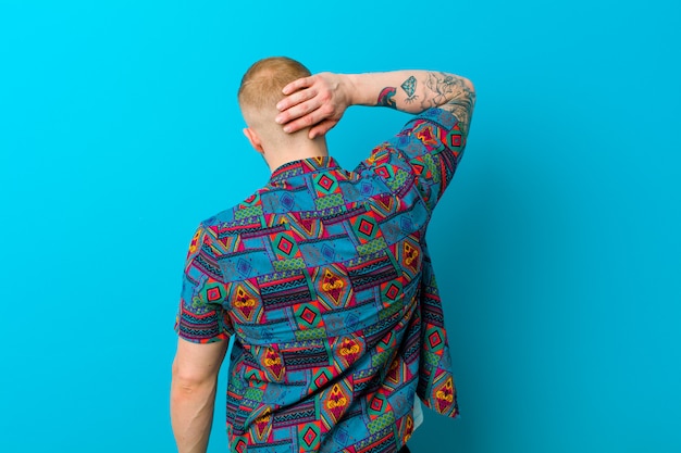 Young blonde man wearing a print shirt thinking or doubting, scratching head, feeling puzzled and confused, back or rear view