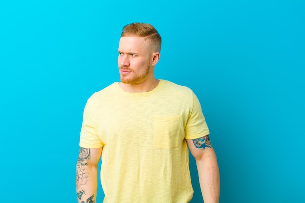 Young blonde man wearing yellow t shirt looking worried, stressed, anxious and scared, panicking and clenching teeth