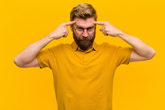 Young blonde man with a serious and concentrated look, brainstorming and thinking about a challenging problem  orange wall