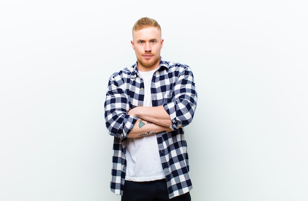 Young blonde man with squared shirt feeling displeased and disappointed, looking serious, annoyed and angry with crossed arms