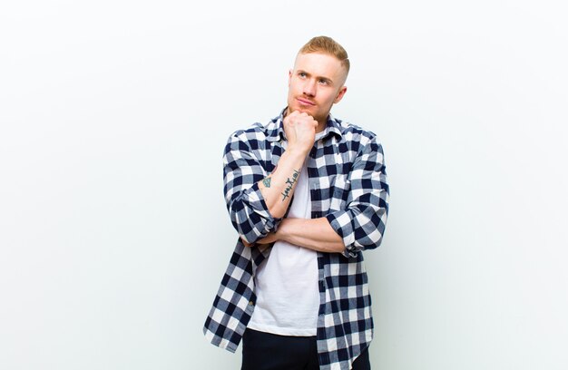 Young blonde man with squared shirt feeling thoughtful, wondering or imagining ideas, daydreaming and looking up to copy space