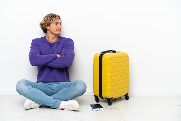 横向きの位置で床に座っているスーツケースを持つ若いブロンドの男