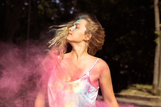 Young blonde model with long curly hair fluttering on wind with Holi dry paint