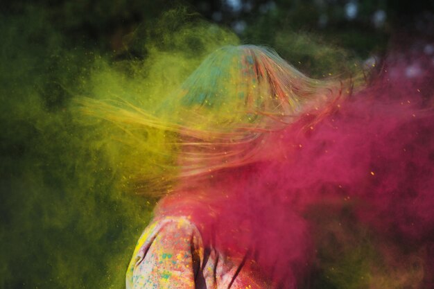 Photo young blonde model with wind in hair playing with exploding yellow and pink dry powder at the holi festival