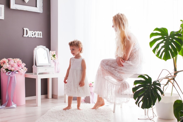 The young blonde mom sits on a white stool in front of her daughter and they are happy with each other