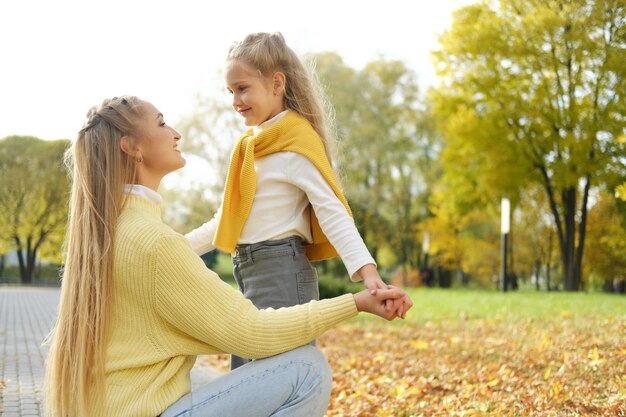 若い金髪の母親がひざまずいて女の子の娘の手を繋いでいる