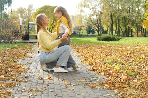 young blonde mother kneeling and hugging the girl daughter in the park on a sunny day