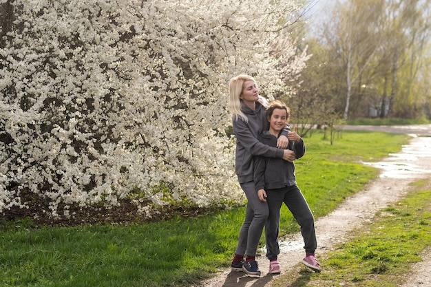 Young blonde mother with child next to flowering tree. Blossom tree and mom with daughter.