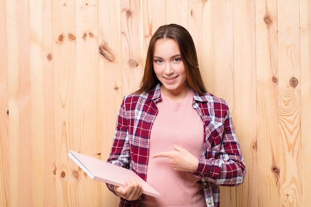 Young blonde pretty girl with a book against wood wall