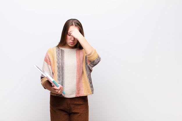 Young blonde pretty girl with books against white wall