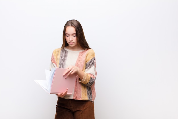 Young blonde pretty girl with books against white wall