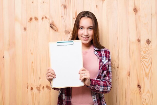 Young blonde pretty girl with a paper sheet against wood wall