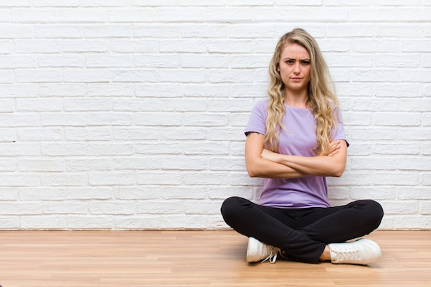 Young blonde pretty woman feeling displeased and disappointed, looking serious, annoyed and angry with crossed arms