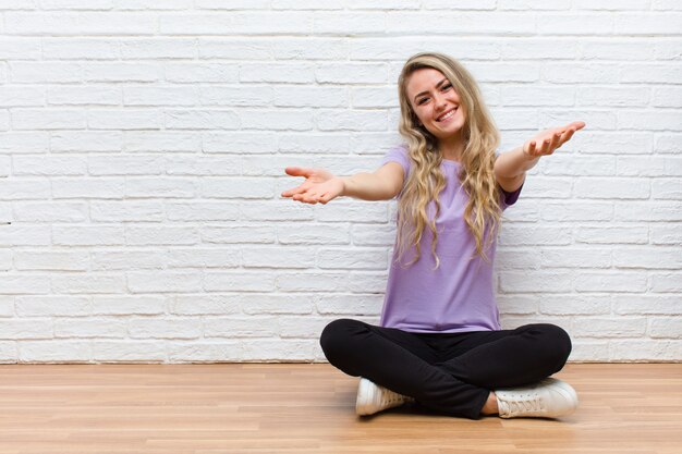 Young blonde pretty woman smiling cheerfully giving a warm, friendly, loving welcome hug, feeling happy and adorable