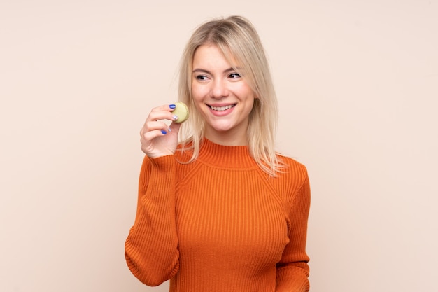 Young blonde Russian woman over isolated wall holding colorful French macarons