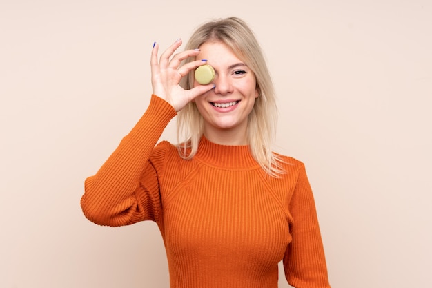 Young blonde Russian woman over isolated wall holding colorful French macarons