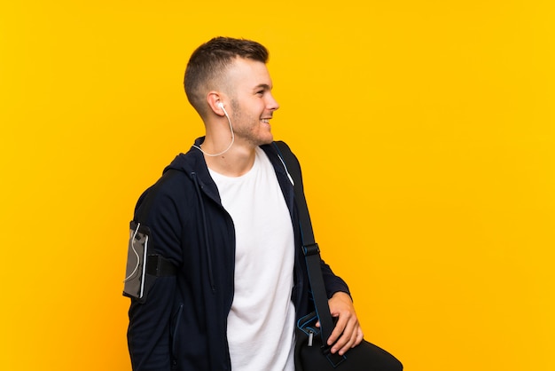 Young blonde sport man over isolated yellow wall looking side