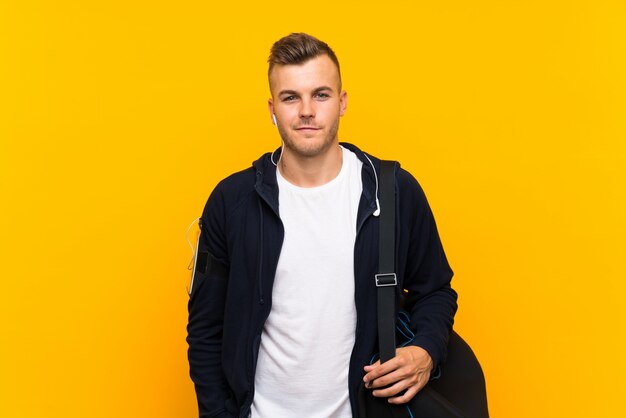 Young blonde sport man over isolated yellow wall smiling a lot