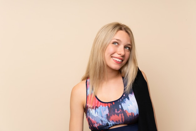 Young blonde sport woman over isolated wall laughing and looking up