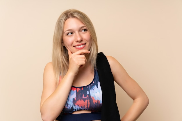 Young blonde sport woman over isolated wall thinking an idea