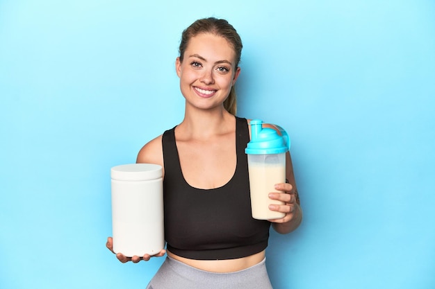 Young blonde sportswoman holding a protein shake in a studio