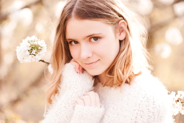 Young blonde teen girl with short haircut posing with blooming tree