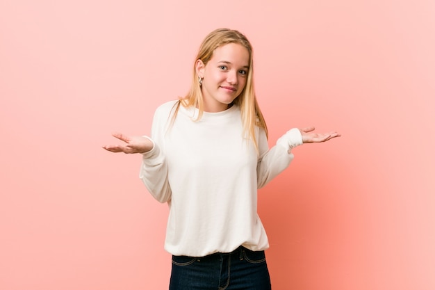 Young blonde teenager woman doubting and shrugging shoulders in questioning gesture.