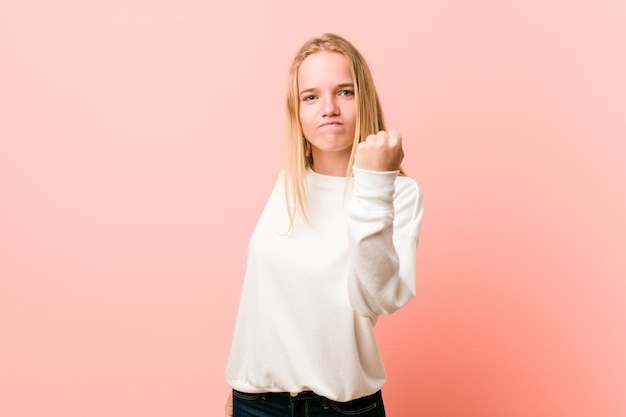 Young blonde teenager woman showing fist to with aggressive facial expression.