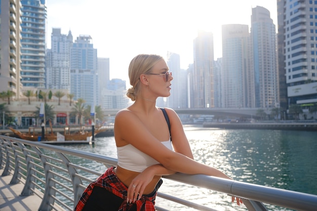 Young blonde travel woman walking on the street outdoors in Dubai city. Dubai marina in United Arab Emirates. UAE summer destination.