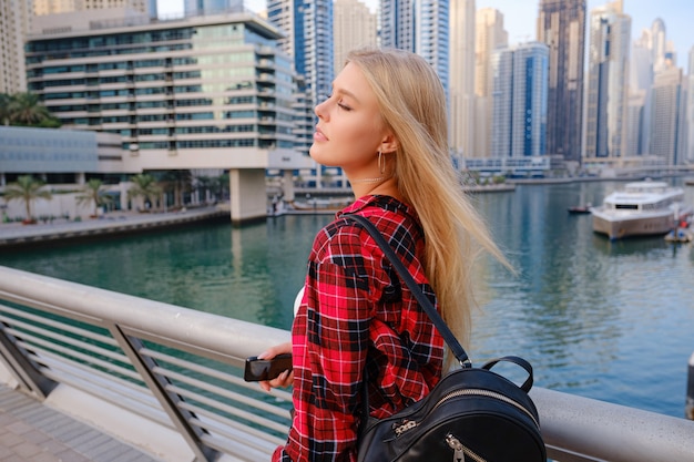 Young blonde travel woman walking on the street outdoors in Dubai city. Dubai marina in United Arab Emirates. 