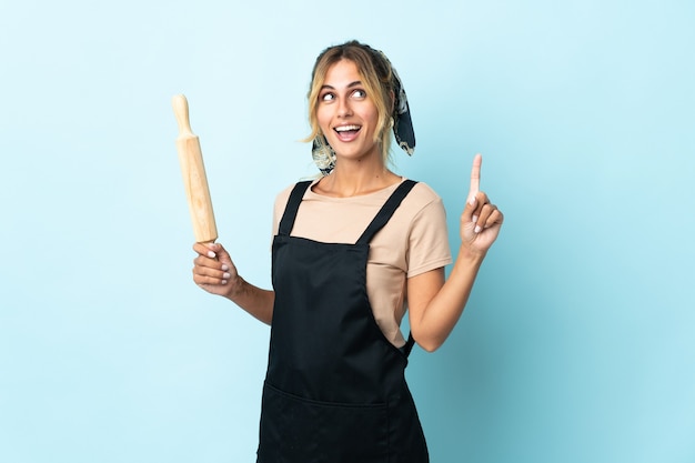 Young blonde Uruguayan cooking woman isolated on blue wall pointing up a great idea