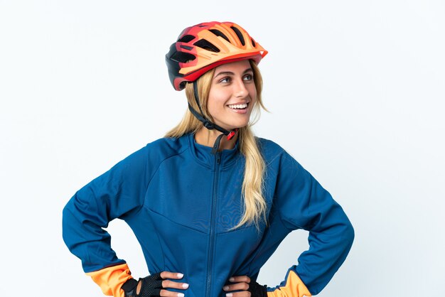 Young blonde Uruguayan cyclist woman isolated on wall posing with arms at hip and smiling