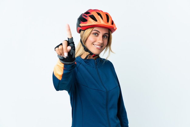 Young blonde Uruguayan cyclist woman isolated on wall showing and lifting a finger