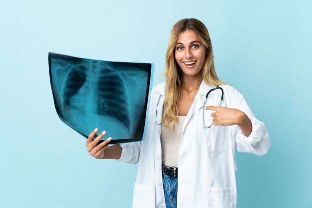 Young blonde Uruguayan doctor woman isolated on blue wall with surprise facial expression