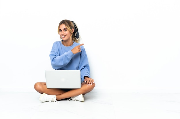 Young blonde Uruguayan girl with the laptop isolated on white pointing to the side to present a product