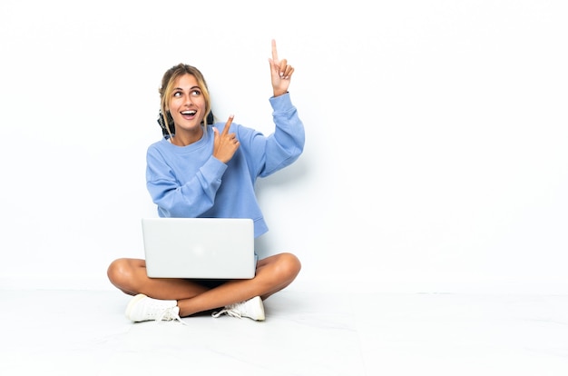 Young blonde Uruguayan girl with the laptop isolated on white wall pointing with the index finger a great idea