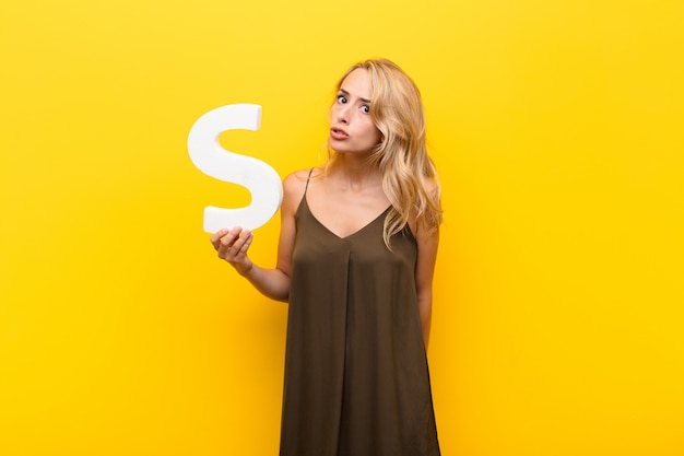 Young blonde woman angry, anger, disagreement, holding the letter S of the alphabet to form a word or a sentence.
