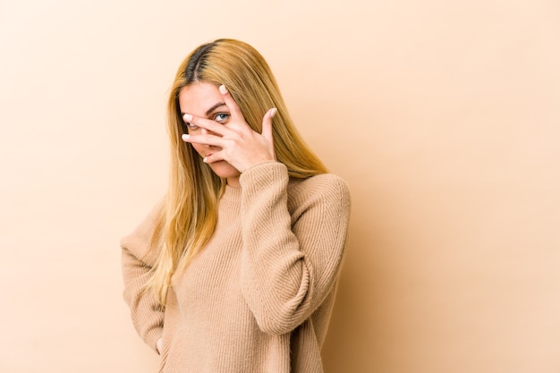 Young blonde woman blinking embarrassed covering face