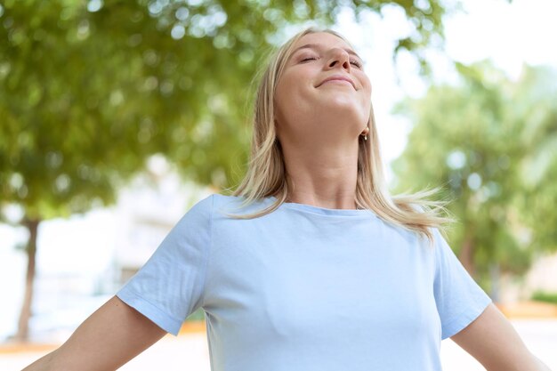 Young blonde woman breathing with arms open at park